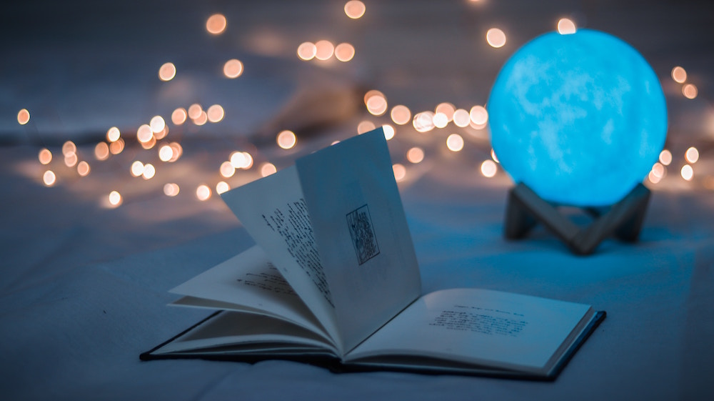 Ein aufgeschlagenes Buch vor einer Kristallkugel und dahinter verschwommene Lichter