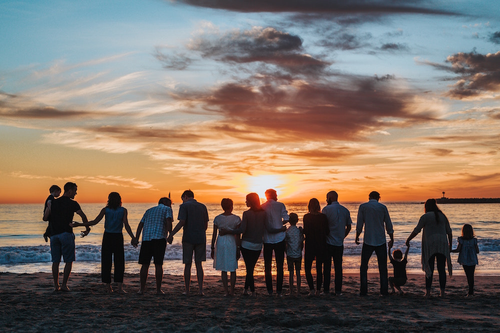 Gruppe von zirka 12 Menschen, von hinten fotografiert, die in der Abenddämmerung nebeneinander stehen und aufs Meer blicken